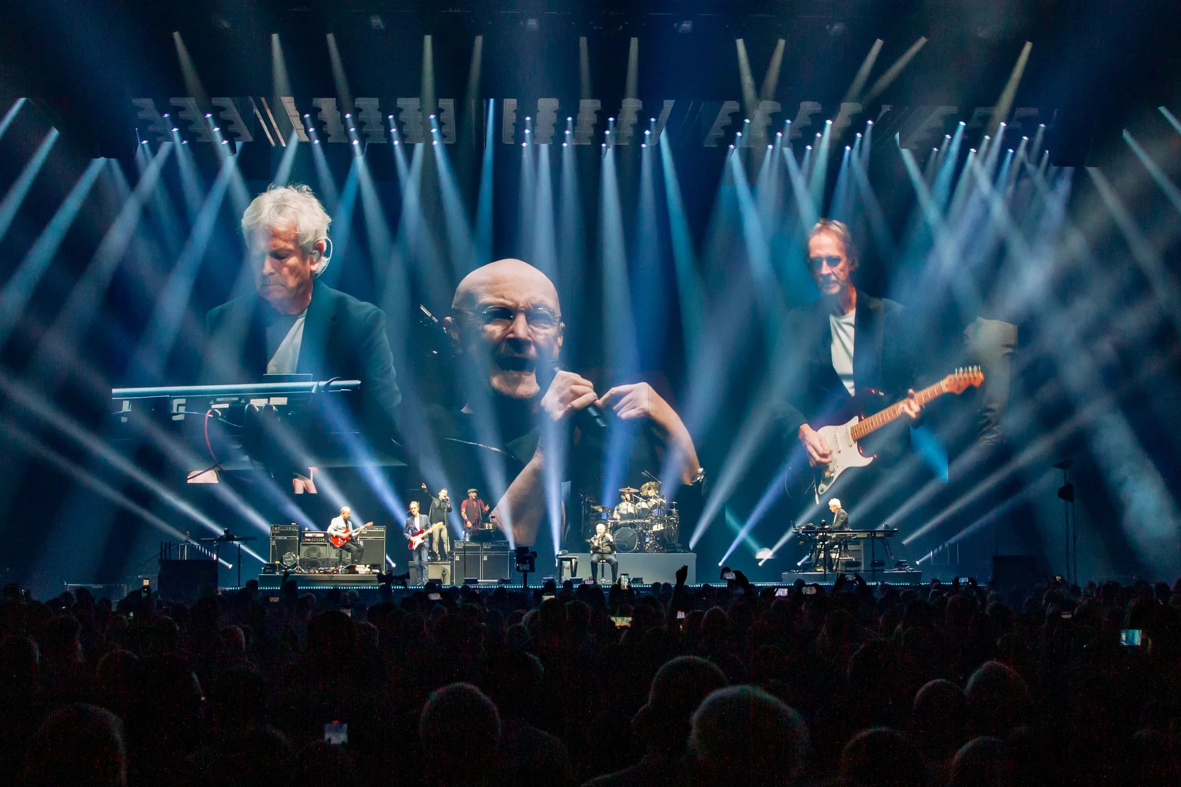 Tony Banks, Phil Collins, and Mike Rutherford on the video screens at Capital One Arena